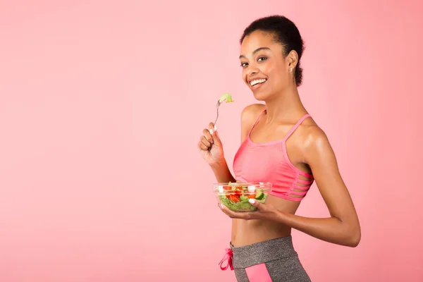 Fekete lány eszik vegetáriánus saláta rózsaszín stúdió háttér — Stock Fotó