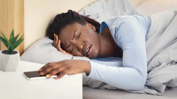 Frau mit Kopfschmerzen schaltet Wecker im Schlafzimmer aus, Panorama — Stockfoto