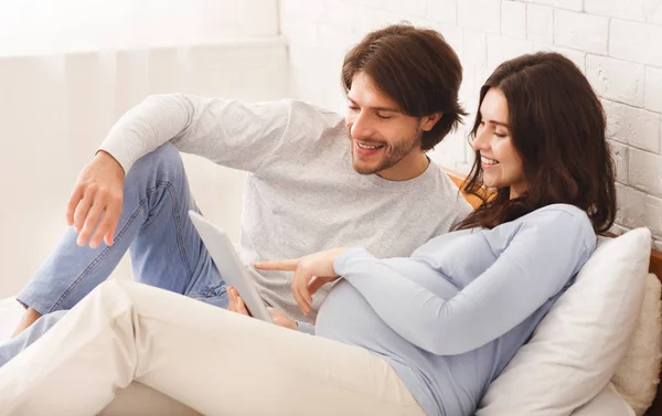 Gravid kvinna och hennes man som använder digitala tabletter i sängen — Stockfoto