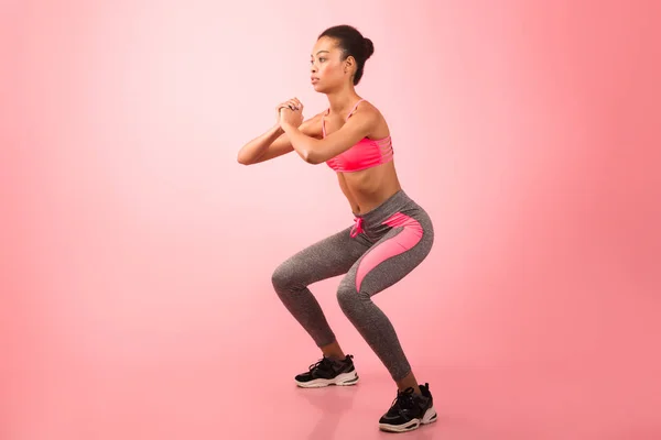Afro ragazza fare profondo squat esercizio su rosa sfondo — Foto Stock