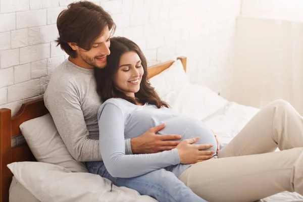 Młoda kobieta w ciąży odpoczywająca w łóżku z mężem — Zdjęcie stockowe