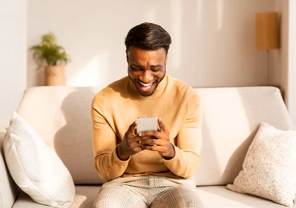 Afro Guy Using Cellphone Playing Games Sitting On Couch Indoor