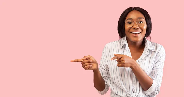 Sorrindo afro mulher apontando os dedos fora de pé sobre fundo rosa — Fotografia de Stock