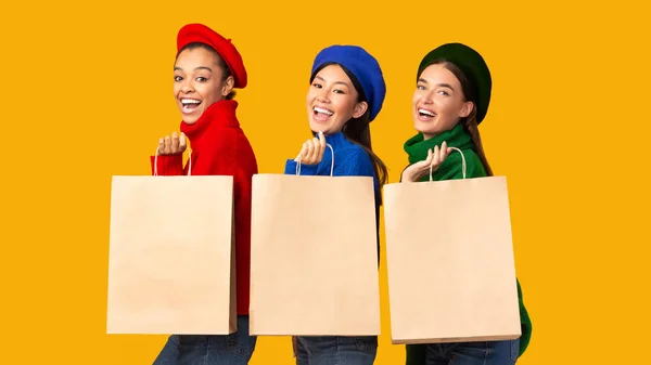 Trois joyeuses filles diverses tenant des sacs Shopper sur fond jaune — Photo