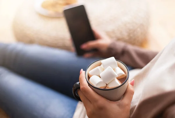 Mulher desfrutando de cacau com marshmallow e usando celular — Fotografia de Stock