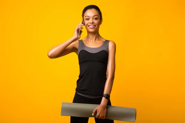 Afro Girl hablando por teléfono sosteniendo estera de yoga, fondo amarillo —  Fotos de Stock