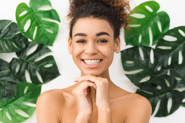 Happy afro woman with natural makeup posing over tropical leaves