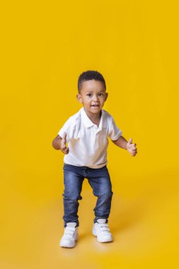 Sevimli afro çocuk sarı arka planda baş parmak hareketi yapıyor.