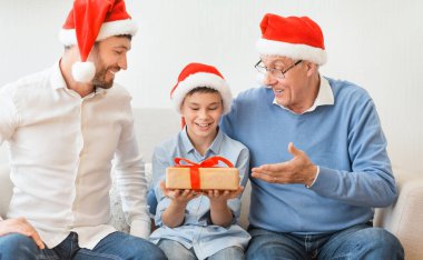 Baba ve büyükbabadan Noel hediyesi alan çocuk içeride oturuyor.