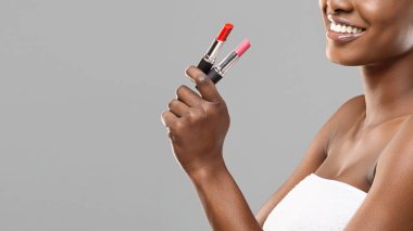 Elinde kırmızı ve pembe ruj tutan tanımlanamayan gülümseyen afro kadın.