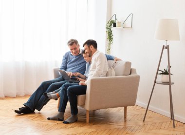 Çocuk, baba ve büyükbaba dizüstü bilgisayar kullanıyor. Evde birlikte oturuyorlar.