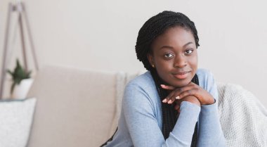 Güzel bir kadın evdeki kanepede dinleniyor ve kameraya gülümsüyor.