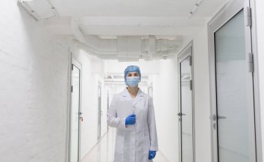 Koruyucu tıp giysileri içinde genç bir kadın doktor boş laboratuvar koridorlarından geçiyor.