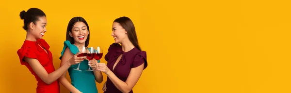 Trois femmes cliquetis verres à vin rouge riant debout, fond jaune — Photo