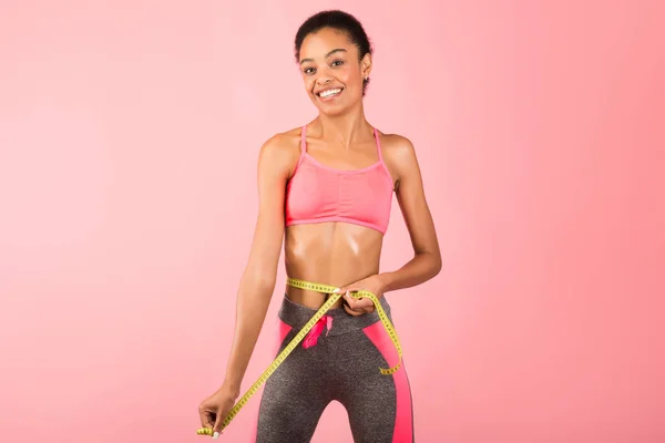 Fit Afro Girl medir a cintura com fita de pé, fundo rosa — Fotografia de Stock