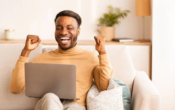 Hombre negro usando el gesto del ordenador portátil Sí sentado en el sofá interior — Foto de Stock