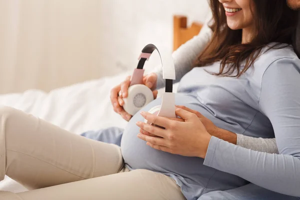 Esperando casal segurando fones de ouvido perto da barriga grávida, tocando música para o bebê — Fotografia de Stock