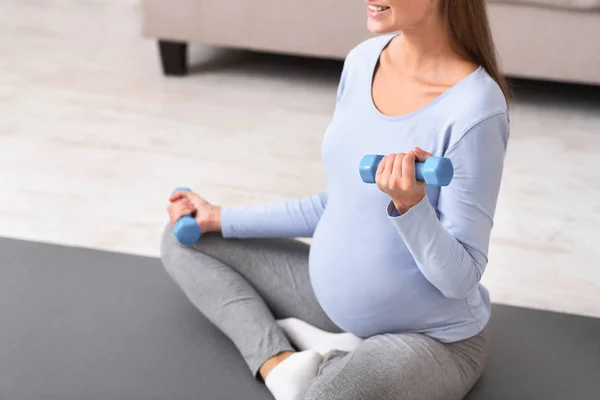 Невизначена вагітна жінка з гантелями на йога килимок — стокове фото