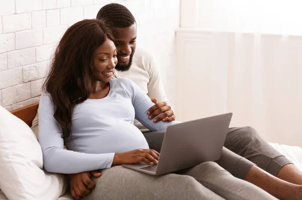 Femme enceinte et son mari à l'aide d'un ordinateur portable, couché sur le lit — Photo