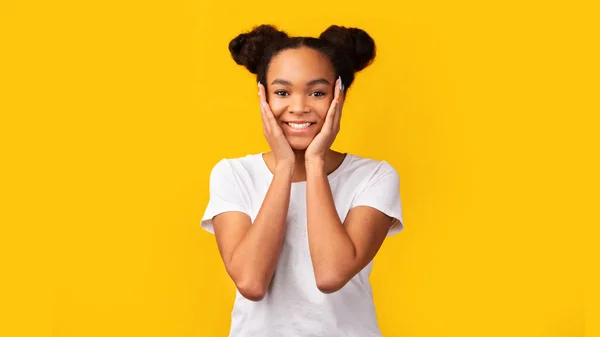 Smiling black teenager holding cheeks on yellow background — ストック写真