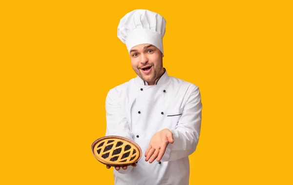 Positive Koch Bäcker Mann zeigt Kuchen stehen auf gelbem Hintergrund — Stockfoto