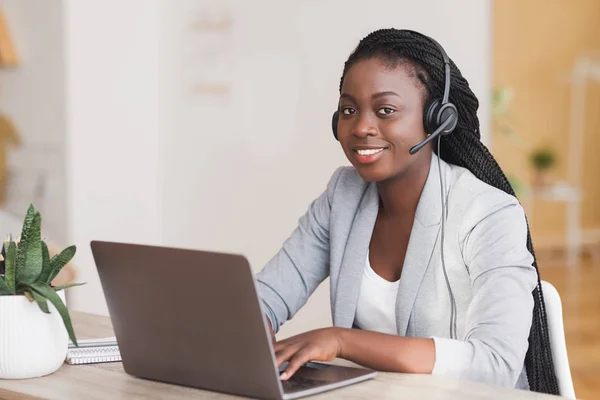 Operadora de soporte al cliente africana que usa auriculares y trabaja en computadora portátil — Foto de Stock