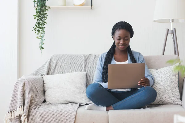 Μαύρη χιλιετή γυναίκα που εργάζεται με φορητό υπολογιστή στον καναπέ στο σπίτι — Φωτογραφία Αρχείου