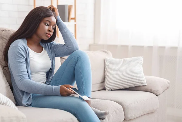 Upprörd Afro Girl sitter på soffan med mobiltelefon, tänker på något — Stockfoto