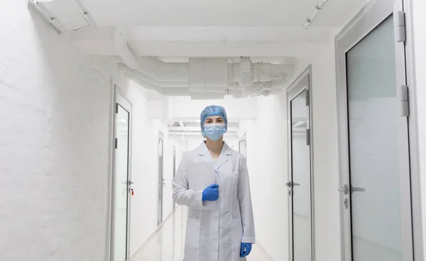 Jovem médica em vestuário médico de proteção passando por corredor de laboratório vazio — Fotografia de Stock