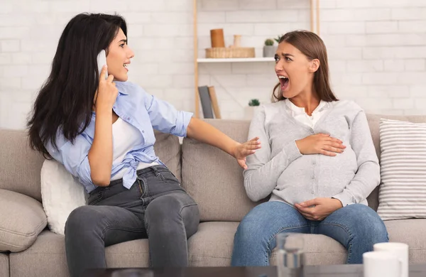 Embarazada chica gritando, su amigo llamando doctor sentado en sofá — Foto de Stock