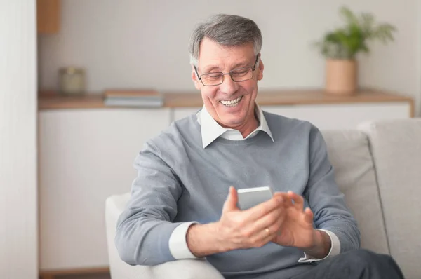 Hombre mayor usando el teléfono celular navegando por Internet sentado en el sofá interior — Foto de Stock