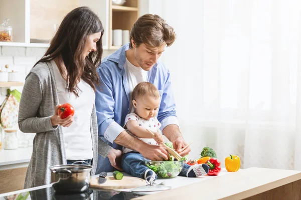 Lindo bebé niño preparando ensalada de verduras con los padres en la cocina — Foto de Stock