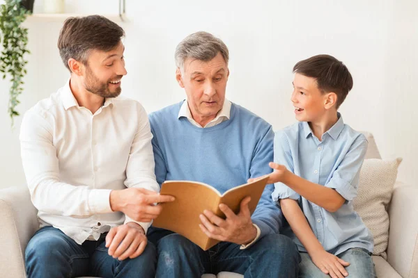 Дідусь читає книгу зі зрілим сином і онуком вдома — стокове фото
