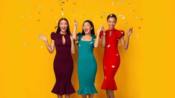 Trois filles de partie debout sous les confettis d'argent tombant, fond jaune — Photo