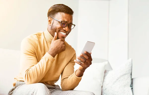 Afrikanisch-amerikanischer Mann, der SMS per Smatphone verschickt und drinnen lacht — Stockfoto