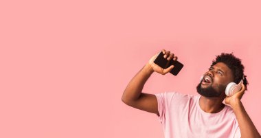 Neşeli Afrikalı adam müzik dinliyor ve akıllı telefonla şarkı söylüyor.