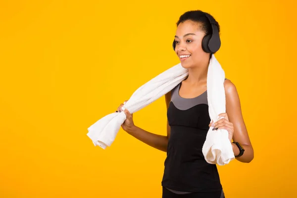 Menina preta em fones de ouvido segurando toalha de pé no fundo amarelo — Fotografia de Stock