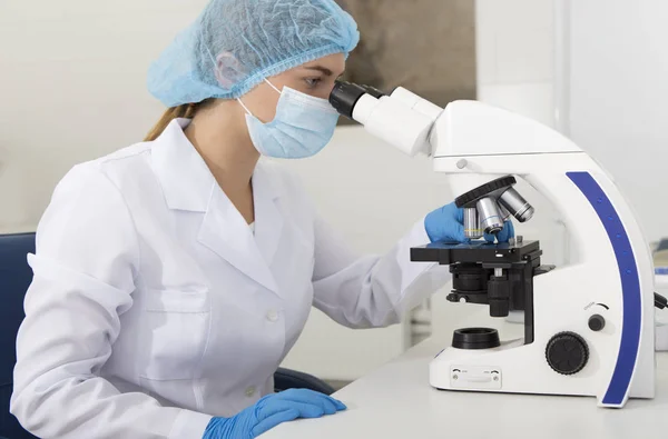 Young medical worker looking on samples through microscope — Stock Photo, Image