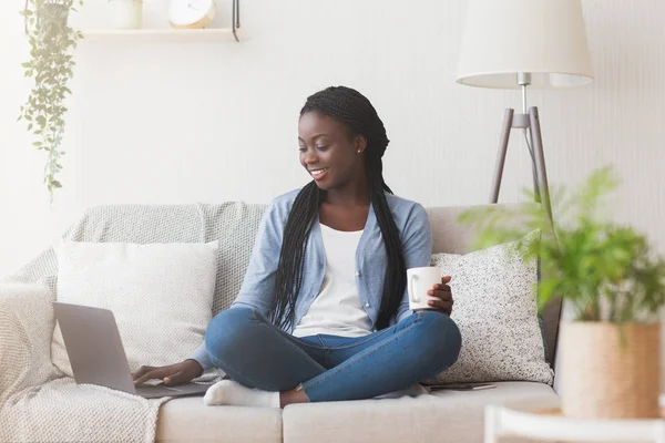 Afro κορίτσι χρησιμοποιώντας το φορητό υπολογιστή στον καναπέ στο σπίτι, Αναζήτηση εργασίας σε απευθείας σύνδεση — Φωτογραφία Αρχείου