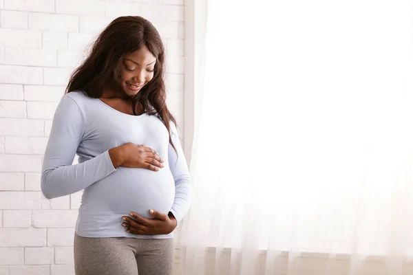 Tranquilla donna afro incinta che abbraccia la pancia a casa — Foto Stock