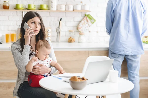 Serious business mom talking on phone, working from home with baby — Stock Photo, Image