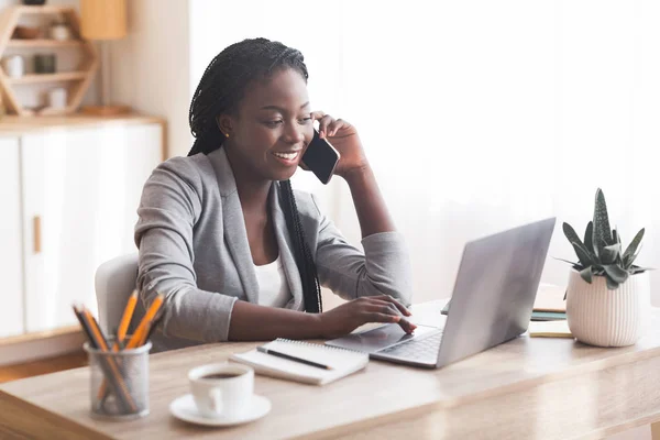 Upptagen svart affärskvinna arbetar i Office med smartphone och bärbar dator. — Stockfoto