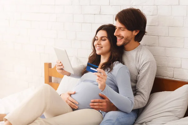 Casal feliz esperando bebê e fazer compras on-line na cama em casa — Fotografia de Stock