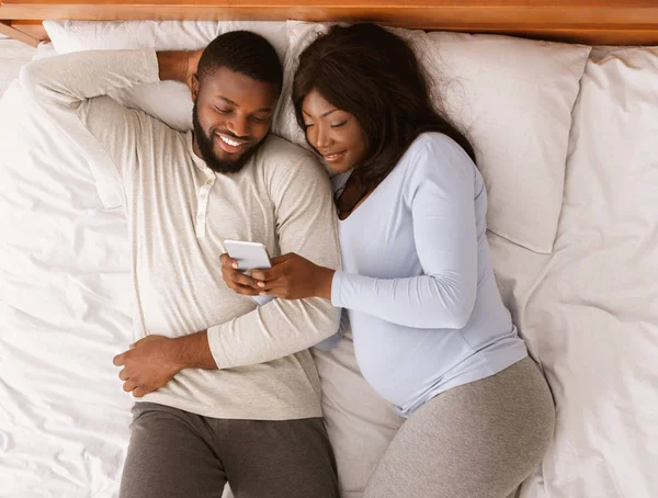 Zwanger paar rusten in bed, kijken naar foto 's op mobiele telefoon — Stockfoto