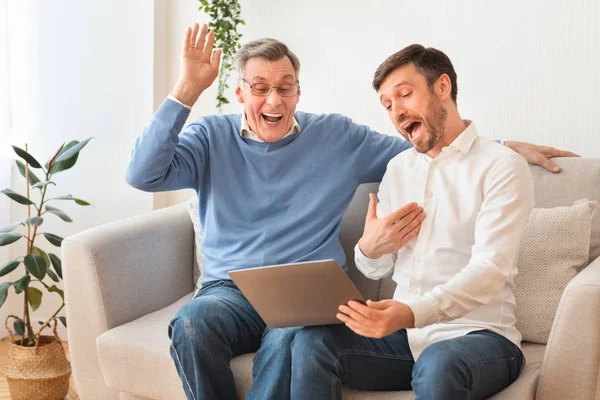 Dojrzałe mężczyzna i starszy ojciec za pomocą laptopa śmiejąc siedzi wewnątrz — Zdjęcie stockowe