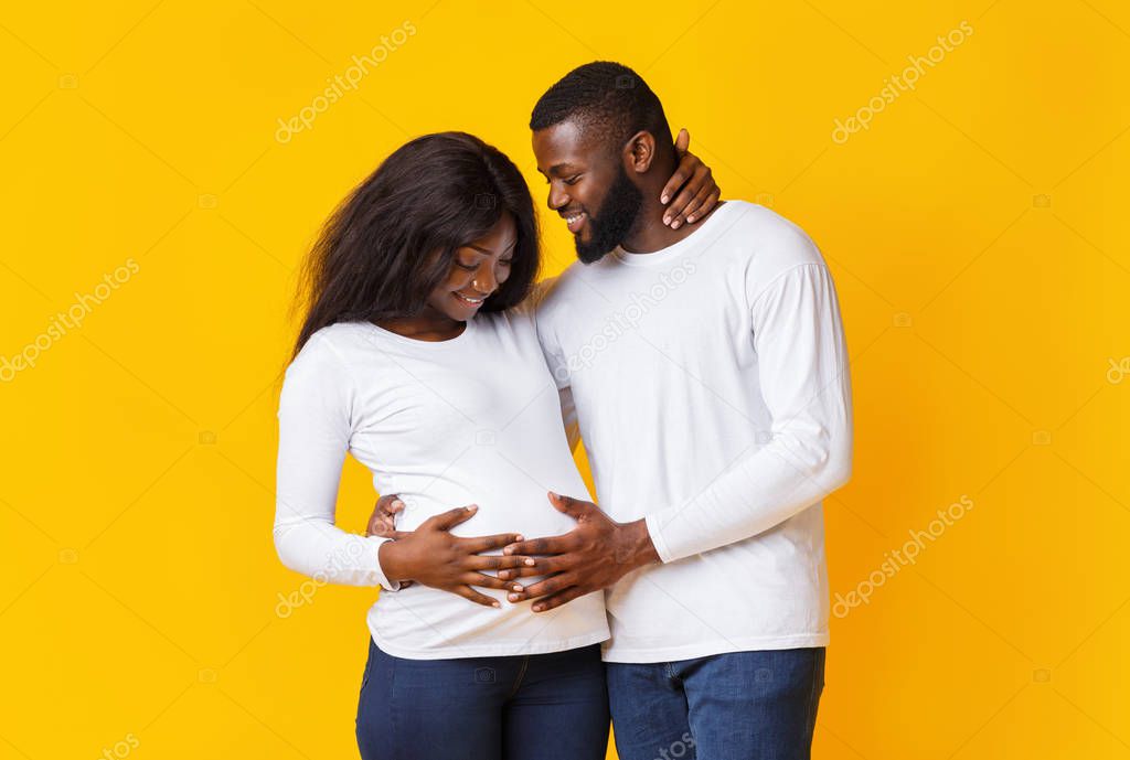 Pregnant couple in love hugging and talking over yellow background