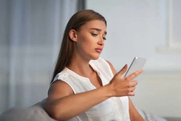 Smutná dívka drží mobil sedí na pohovce doma — Stock fotografie