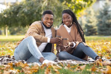 Romantik çift, sonbahar parkında ekose üzerinde oturup kahve içiyorlar.