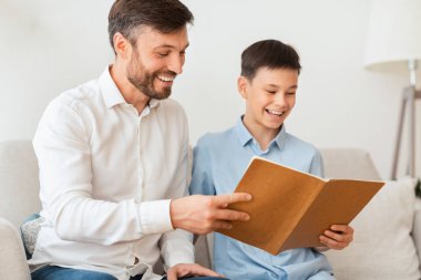 Oğlan ve baba evde koltukta oturmuş kitap okuyorlar.