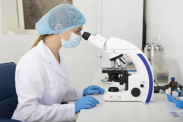 Orvosi ruhában dolgozó fiatal nő mikroszkóppal — Stock Fotó